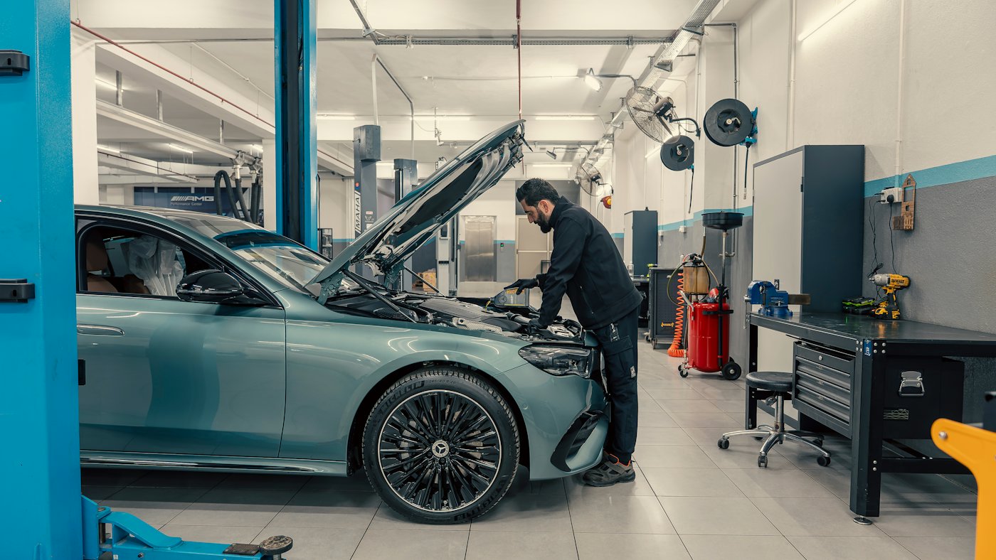 A mechanic working on a car with the hood open in a repair shop