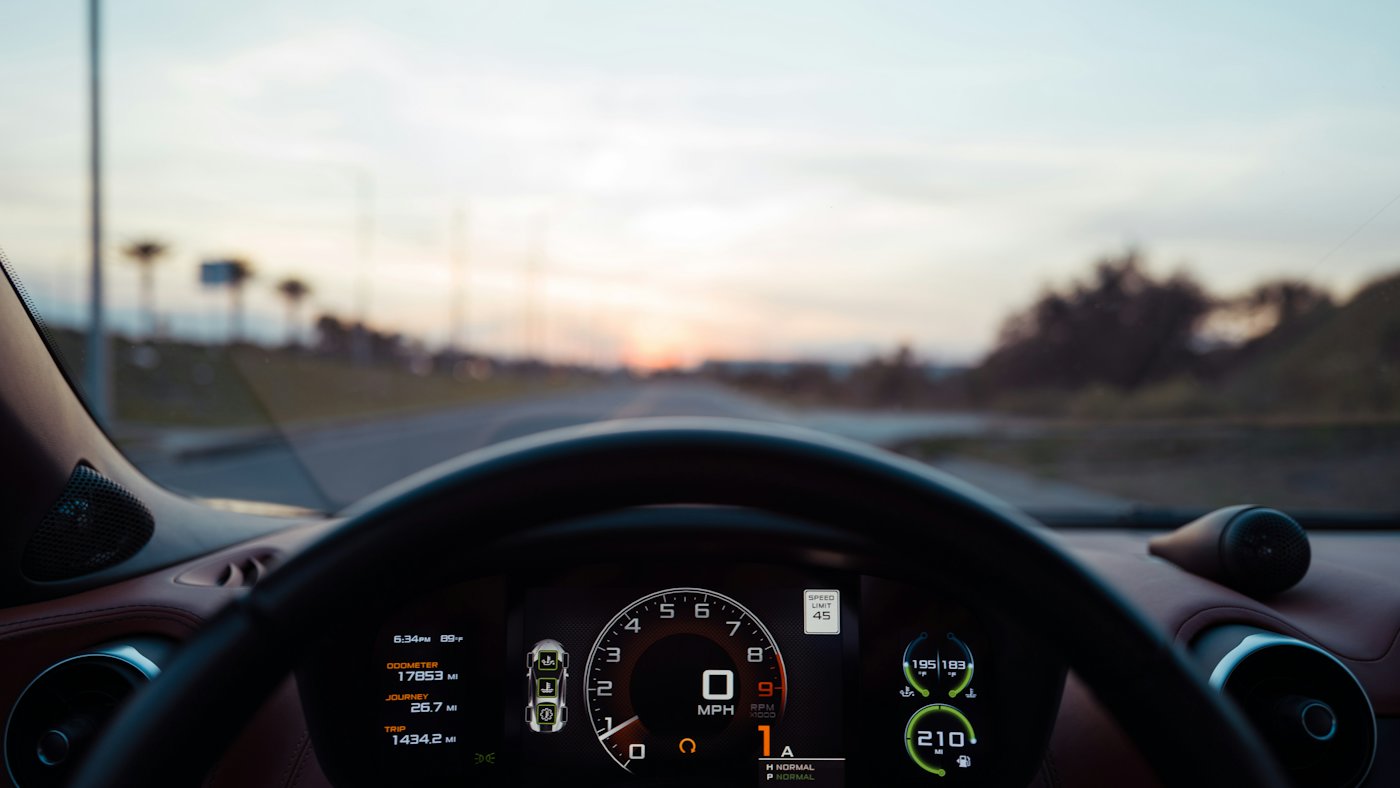 A car dashboard showing the odometer and speedometer at sunset